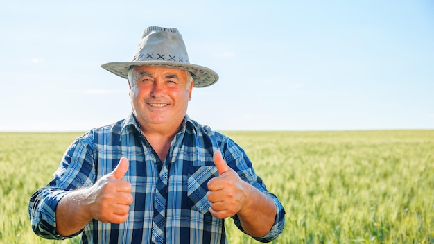 Trabajador masculino de edad avanzada positivo mirando a la cámara con los pulgares hacia arriba mientras está de pie en un campo agrícola