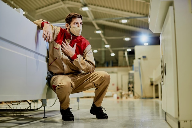 Trabajador masculino con mascarilla y sintiendo dolor mientras trabaja en una fábrica
