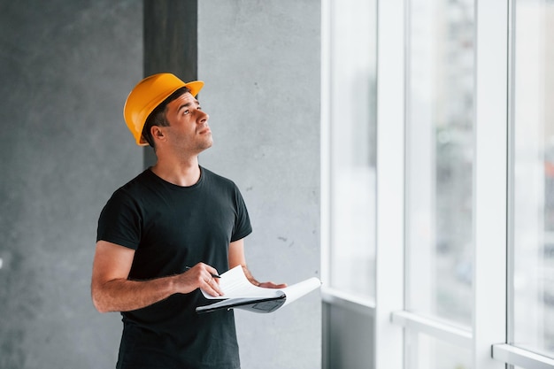 Trabajador masculino o ingeniero con casco amarillo parado en el interior con bloc de notas