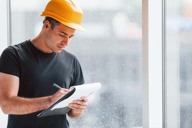 Trabajador masculino o ingeniero con casco amarillo parado en el interior con bloc de notas