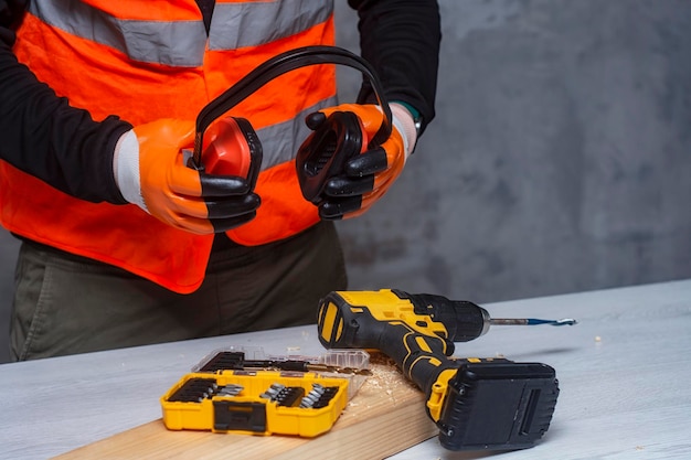 El trabajador masculino sostiene un destornillador inalámbrico eléctrico cerrado en sus manos contra el fondo de una herramienta de construcción y un muro de hormigón