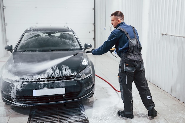 Trabajador masculino en uniforme lavando un auto nuevo y moderno que cubrió con jabón Concepción del servicio