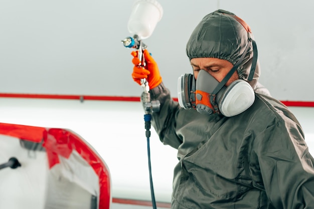Trabajador mecánico de automóviles con ropa de trabajo protectora rociando pintura blanca en una parte del automóvil en el taller