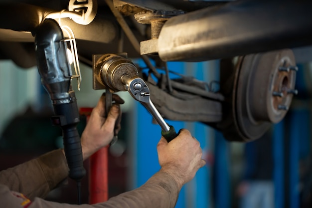 Foto trabajador mecánico reparando la suspensión del automóvil levantado en la estación de taller de reparación de automóviles