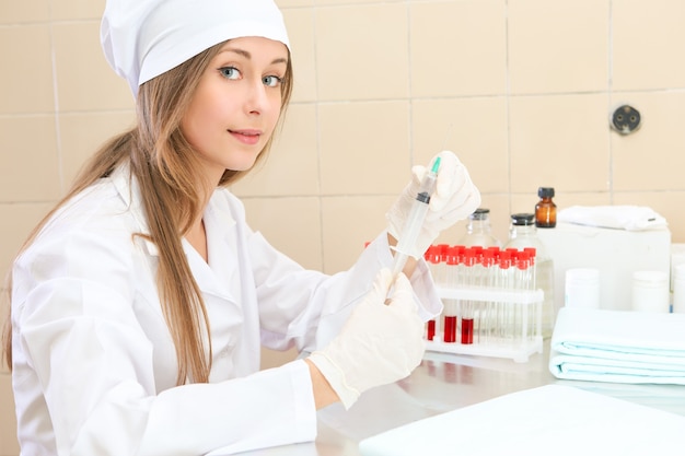 Trabajador médico femenino con tubos de análisis de sangre y jeringa