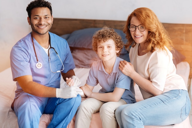 Foto trabajador médico guapo manteniendo una sonrisa en su rostro y sosteniendo la mano lesionada de su paciente