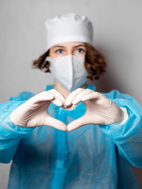 Trabajador médico con una máscara desechable y una bata de laboratorio hace un signo de corazón.