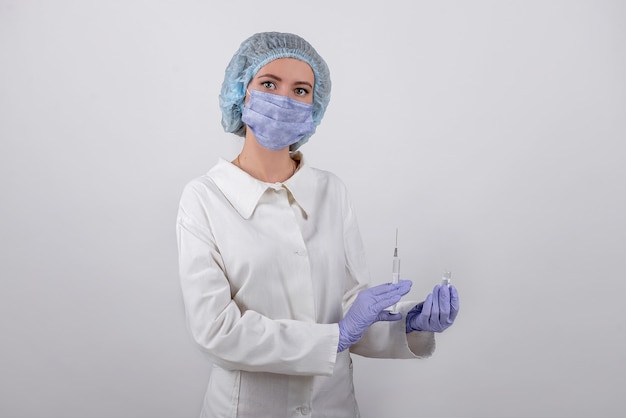 Foto trabajador médico en una máscara, guantes azules y una red sostiene una jeringa y una ampolla en sus manos