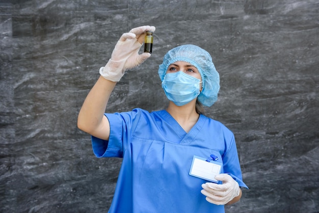 Trabajador médico en uniforme azul sosteniendo ampollas con vacunas de diferente color sobre fondo abstracto