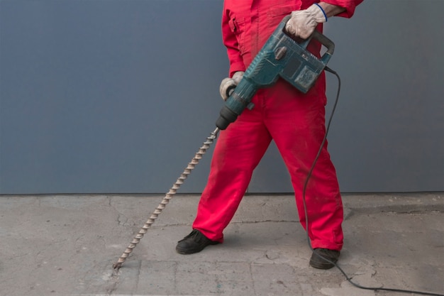 un trabajador en un mono que trabaja con un taladro con un taladro largo destruye el piso de concreto