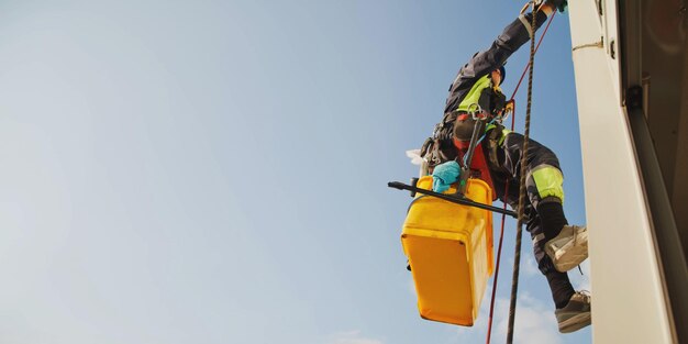 Foto trabajador de montañismo industrial se cierne sobre el edificio de la fachada residencial mientras lava el acristalamiento de la fachada exterior