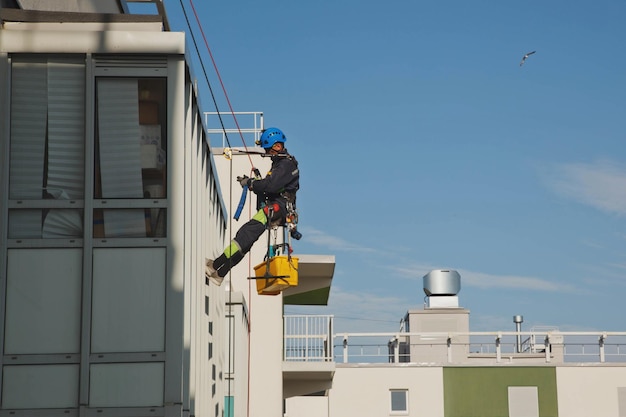 Trabajador de montañismo industrial se cierne sobre el edificio de la fachada residencial mientras lava el acristalamiento de la fachada exterior