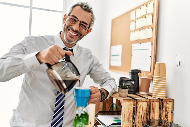 Foto trabajador de negocios de hombre canoso de mediana edad sirviendo café en una taza en la oficina