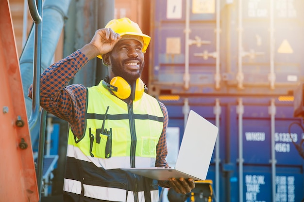 Trabajador negro capataz de ingeniero de trabajo africano en el envío de carga portuaria con computadora portátil