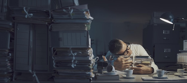 Foto trabajador de oficina agotado y estresado durmiendo en su escritorio está trabajando horas extras hasta tarde en la noche