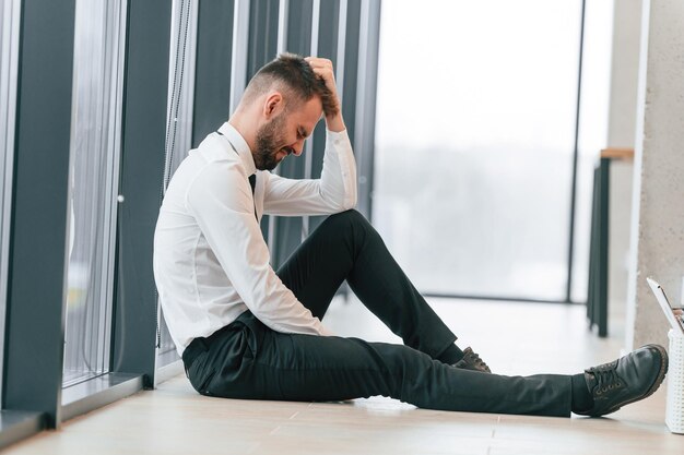 Trabajador de oficina deprimido está sentado en el piso vista lateral