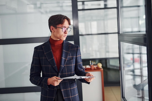 Trabajador de oficina con gafas y ropa formal de pie en el interior.