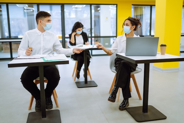 Trabajador de oficina con mascarilla para el distanciamiento social para la prevención de virus mientras usa una computadora portátil.