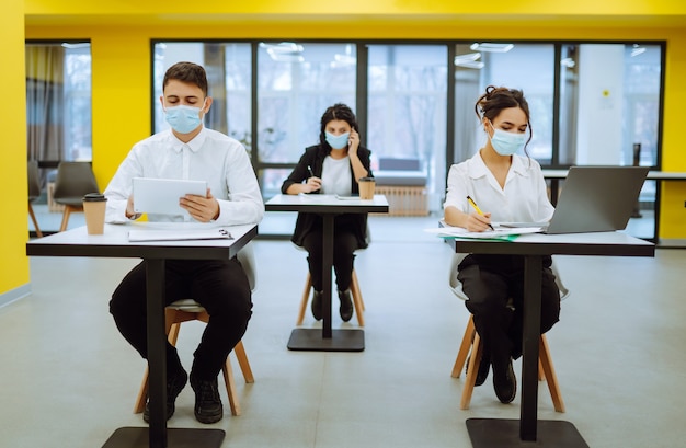 Trabajador de oficina con mascarilla para el distanciamiento social para la prevención de virus mientras usa una computadora portátil.