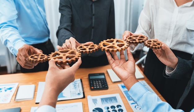 Trabajador de oficina que sostiene la rueda dentada como unidad y trabajo en equipo del sistema en el lugar de trabajo corporativo con montones de documentos comerciales e informes financieros en la mesa de reuniones Gente de negocios con éxito empresarial Concord