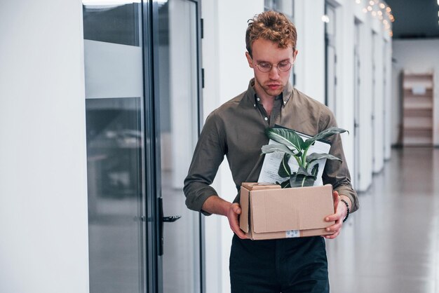 Trabajador de oficina en ropa formal caminando con caja con planta verde en su interior.