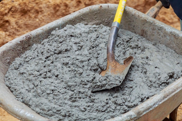 Trabajador palea una mezcla húmeda de concreto de una carretilla en la instalación de bloques de acera