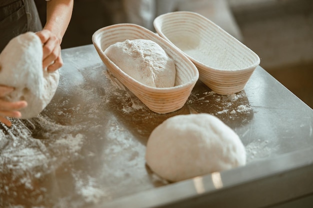 Foto trabajador con pan de masa cruda prepara el pan en la mesa de metal en la panadería