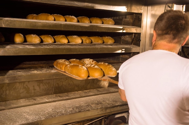 trabajador de panadería sacando panes recién horneados con pala del horno profesional en la fabricación
