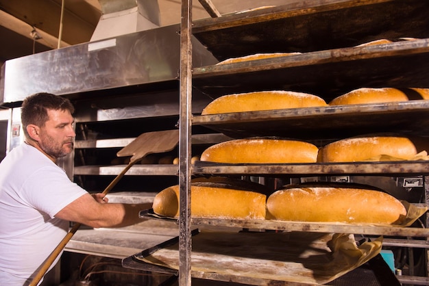 trabajador de panadería sacando panes recién horneados con pala del horno profesional en la fabricación