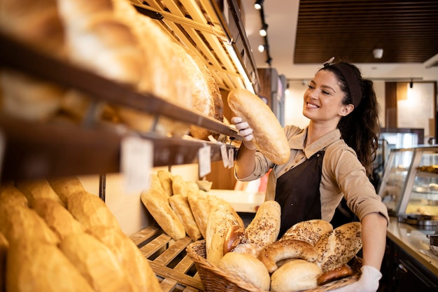 Trabajador de panadería sonriente feliz colocando pan criado en el estante listo para la venta