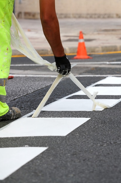 trabajador con pantalones reflectantes quita cinta termoplástica de marcado de obras viales para pintar líneas de tráfico