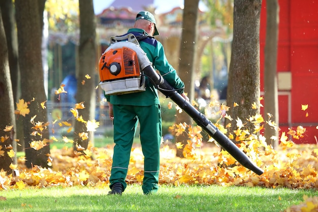 Trabajador en el parque limpia el césped de hojas caídas con la ayuda de una turbina eólica