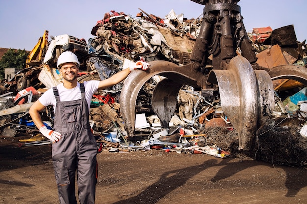 Trabajador de pie junto a la máquina industrial hidráulica utilizada para levantar piezas de chatarra en el depósito de chatarra