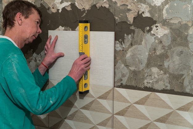 El trabajador pone azulejos en la pared. Trabajos de acabado, enfoque borroso. La tecnología de colocación de baldosas.
