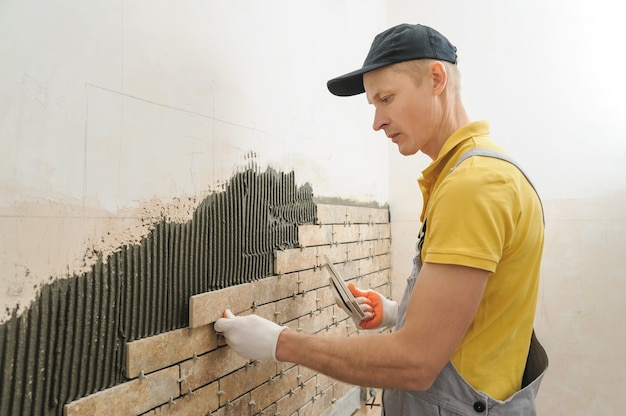 El trabajador poniendo azulejos en forma de ladrillo en la pared