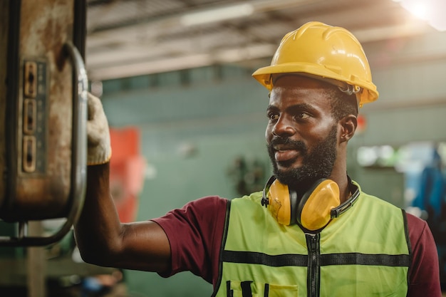 Trabajador profesional africano negro que trabaja en una fábrica de la industria pesada con traje de ingeniero y casco para la máquina de operación de los trabajadores de seguridad