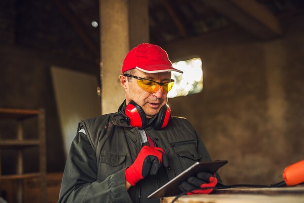 Trabajador profesional moderno de la tela con protección sosteniendo una tableta y comprobando el estado de producción.