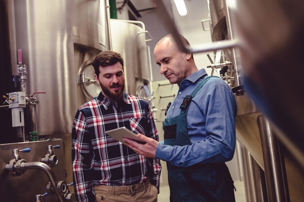 Trabajador y propietario discutiendo sobre tableta digital en cervecería