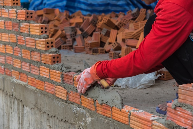 Trabajador que instala el ladrillo rojo para el sitio de construcción