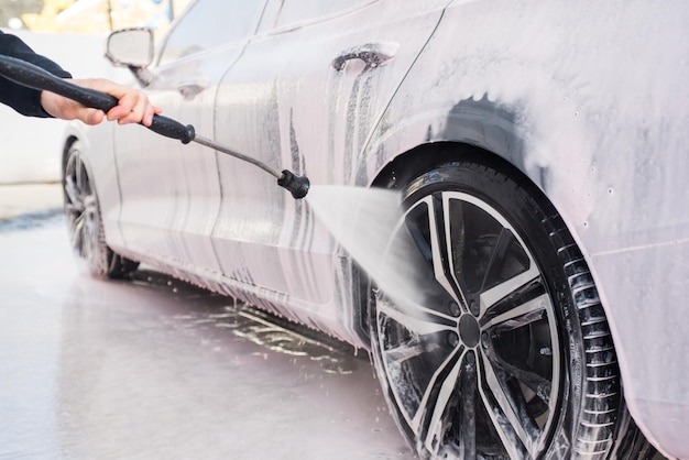 Foto trabajador que limpia el borde del coche con la presión del agua del rociador