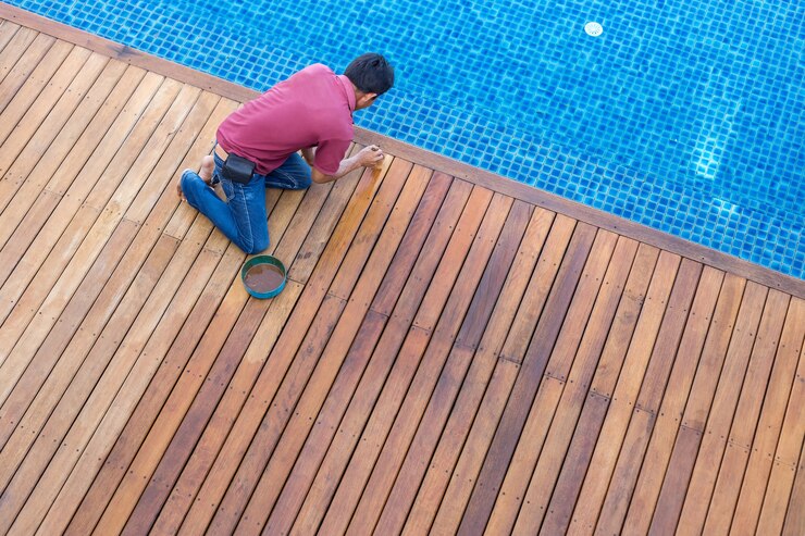 Un trabajador que pinta la cubierta de piscina de madera exterior, visión superior