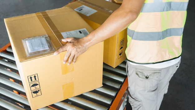 Trabajador que trabaja en un transportador, su clasificación de cajas de cartón para entregar a un cliente. Almacén de distribución, paquetería, envío de mercancías,