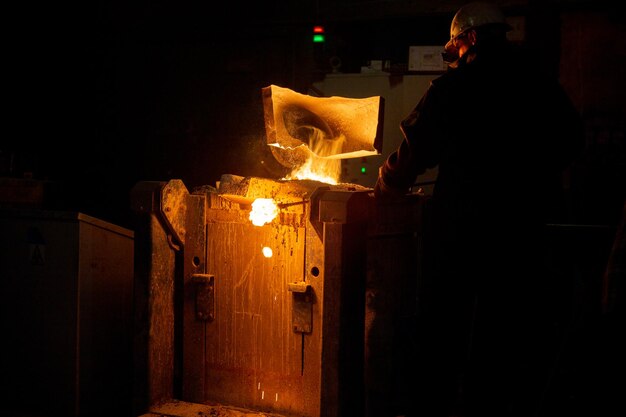 Trabajador quitando escoria de horno metalúrgico con campana extractora y fundiendo metal con vapor