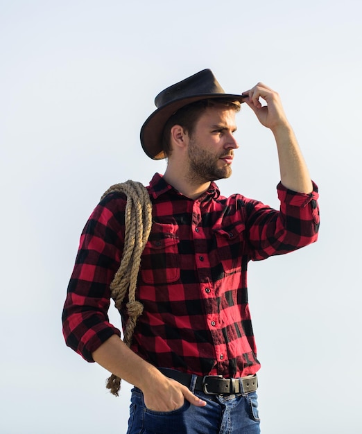 Foto trabajador del rancho vida en el rancho vaquero con fondo de cielo de cuerda de lazo granja ecológica concepto de agricultura hombre guapo con sombrero y atuendo de estilo rústico mantener rancho granjero pensativo pensando en negocios