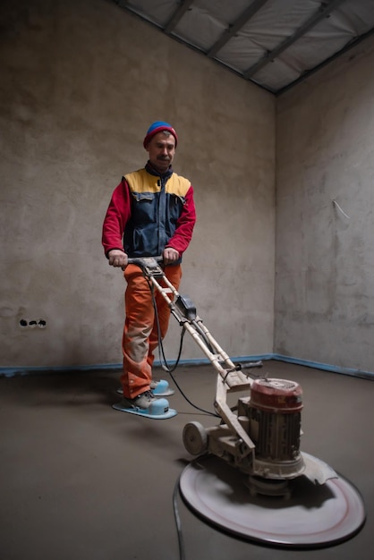 Trabajador realizando y puliendo pisos de arena y cemento en el sitio de construcción de un nuevo apartamento de dos niveles. Solera de suelo de arena y cemento.