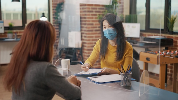 Trabajador de recursos humanos que tiene una cita con el candidato en una entrevista de trabajo durante la pandemia del coronavirus. Mujeres asiáticas con máscaras faciales reunidas para discutir el reclutamiento empresarial y el empleo en el cargo.