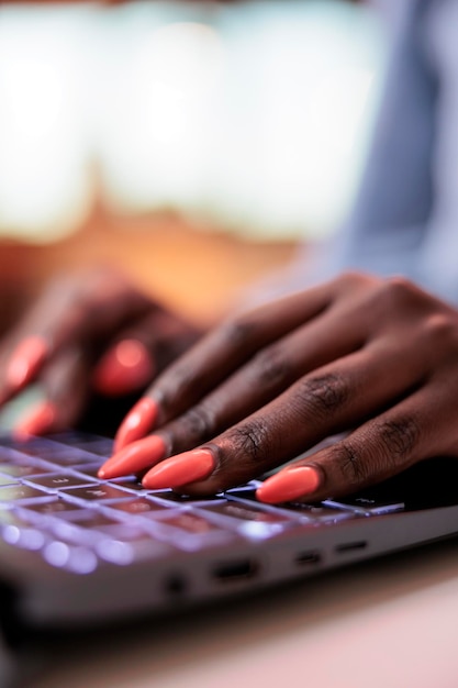 Trabajador remoto de la empresa afroamericana escribiendo un mensaje en el teclado de la computadora portátil, vista cercana de las uñas cuidadas. Joven empleado corporativo, escribiendo correo electrónico en la computadora, concéntrese en las manos