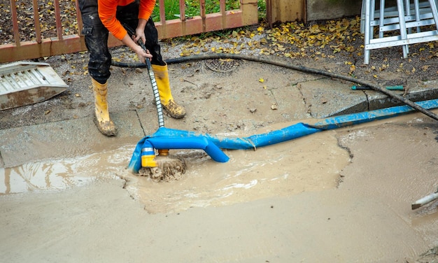 Un trabajador repara una tubería de agua rota en la calle usando una bomba para vaciar la zanja