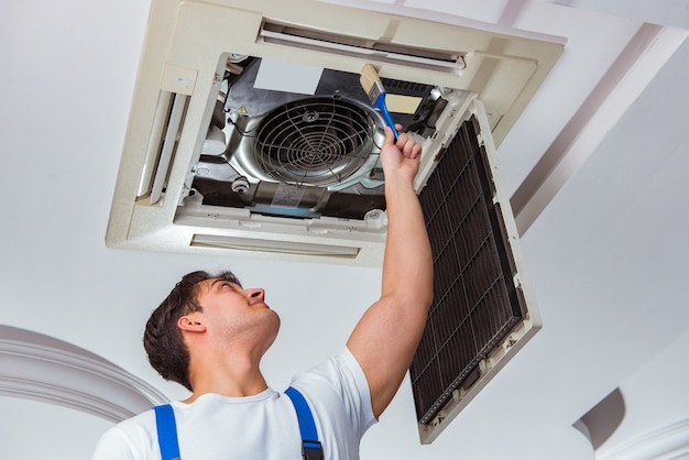 Trabajador reparando unidad de aire acondicionado de techo