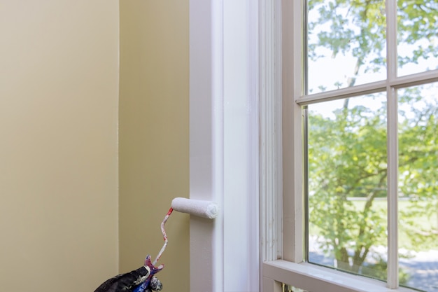 Trabajador de restauración de viviendas pintando con un rodillo de pintura de color blanco una moldura de ventana